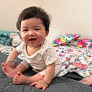 Moana is registered to the contest to win money with this photo: baby, bed, blanket, child, clothing, colorful, cozy, cute, face, happy, home, indoor, infant, person, pillow, portrait, sitting, smiling, soft, toy