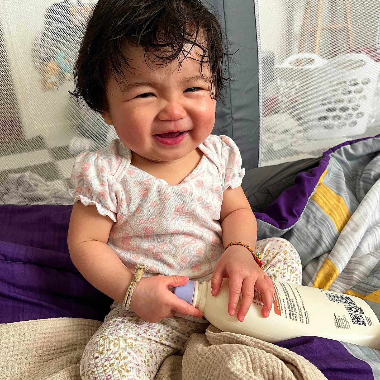 Moana is registered to the contest to win money with this photo: toddler, baby, smiling, happy, bottle, clothing, blanket, indoors, playpen, laundry_basket, bracelet, pajamas, person, child, cute, portrait, sitting, hair, expression, cozy