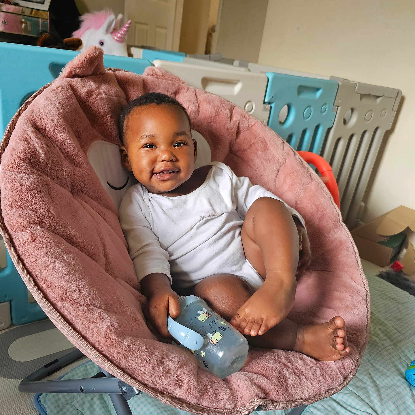 Arbela joined the competition — help win amazing prizes! baby, child, comfortable, cute, floor_mat, furniture, happy, home, indoor, infant, person, pink_chair, playpen, plush, relaxed, sippy_cup, smiling, toy, unicorn_toy, white_clothing