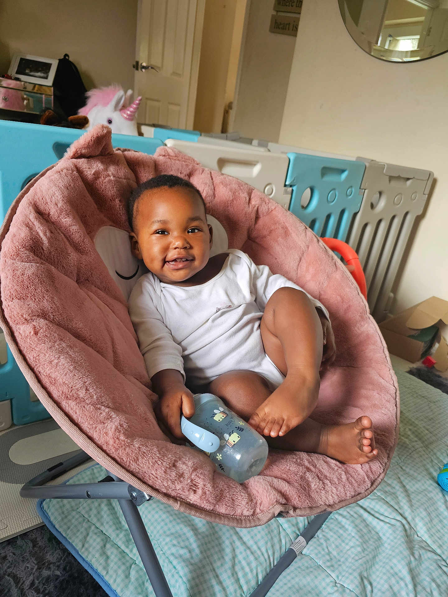 Arbela joined the competition — help win amazing prizes! baby, child, smiling, sippy_cup, pink_chair, plush, indoor, playpen, unicorn_toy, floor_mat, white_clothing, happy, infant, person, furniture, comfortable, home, cute, relaxed, toy