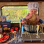 baby, chef_hat, spaghetti, metal_pot, tomatoes, mozzarella, pasta_box, breadsticks, kitchen_utensils, wooden_table, window, greenery, baby_eating, food, cooking, playful, messy, indoor, child, cute