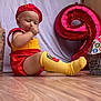 Ezéchias participe au concours pour gagner de l'argent avec cette photo : baby, child, sitting, red_clothing, yellow_clothing, socks, balloon, number_balloon, wooden_floor, toy, curious, indoors, face, hand, footwear, hat, fast_food_theme, playful, cute, portrait