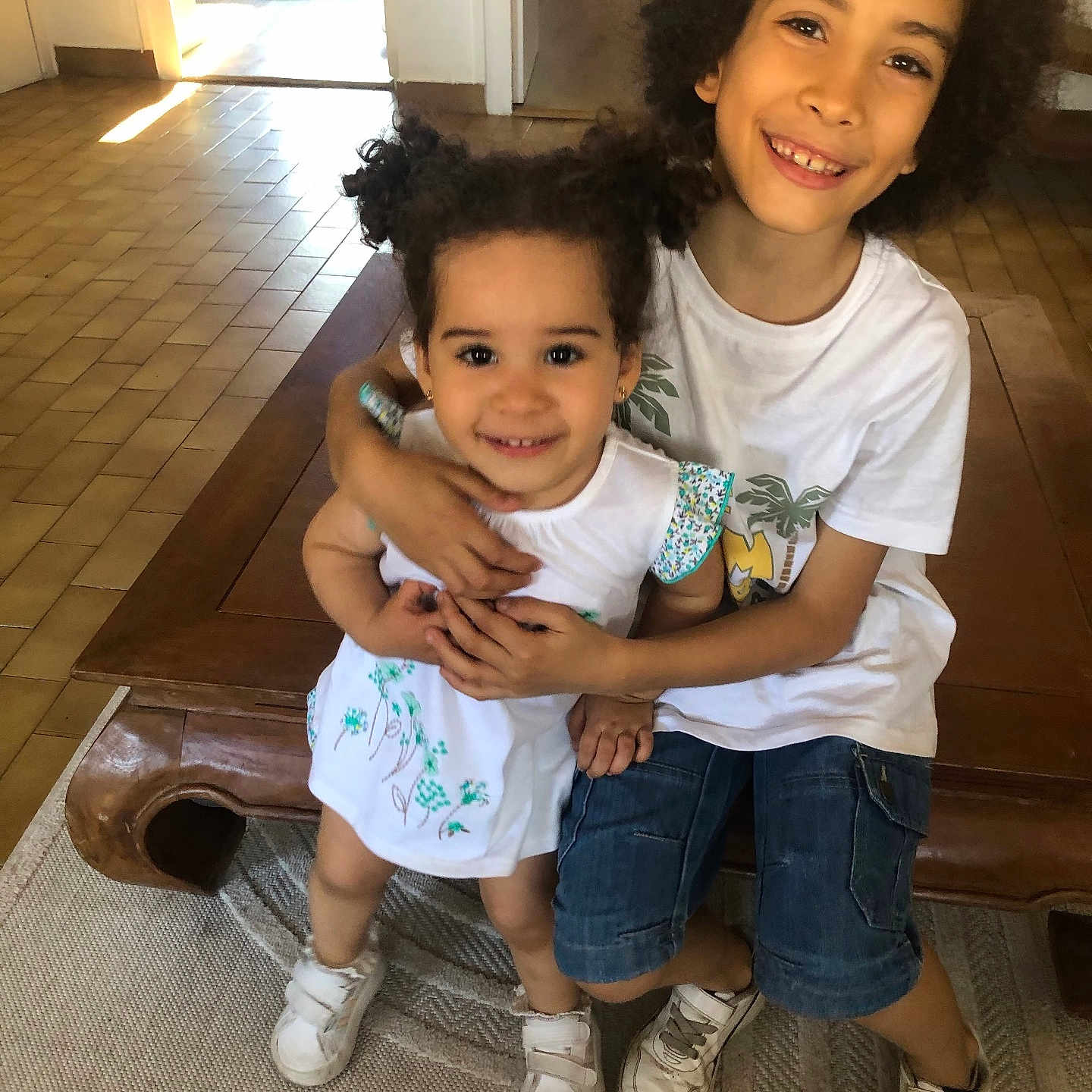 Yara Carneiro participe au concours pour gagner de l'argent avec cette photo : carpet, child, children, curly_hair, denim_shorts, doorway, family, floor_tiles, happy, hug, indoor, pigtails, playroom, portrait, siblings, smile, sneakers, toys, white_shirt, wooden_bench