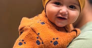 Atharv is registered to the contest to win money with this photo: baby, child, childhood, closeup, cozy, cute, face, hand, happy, headwear, holding, indoor, infant, orange_hat, orange_sweater, paw_prints, person, portrait, smile, warm_clothing