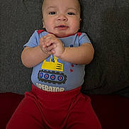 Lucas is registered to the contest to win money with this photo: baby, child, infant, clapping, smiling, blue_shirt, red_pants, excavator, sitting, couch, indoor, face, hands, happy, young, person, casual_clothing, home, portrait, cute