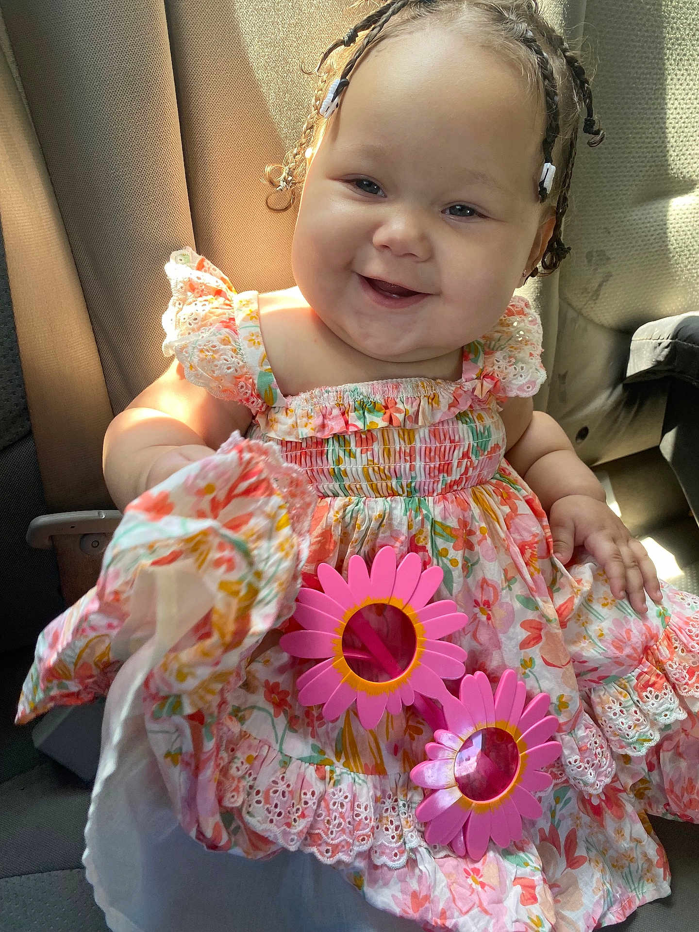 Azariah is registered to the contest to win money with this photo: baby, child, smile, braids, hair_clips, dress, floral_pattern, sunglasses, pink, car_seat, sunlight, happy, cute, infant, portrait, clothing, hand, seat, indoors, person