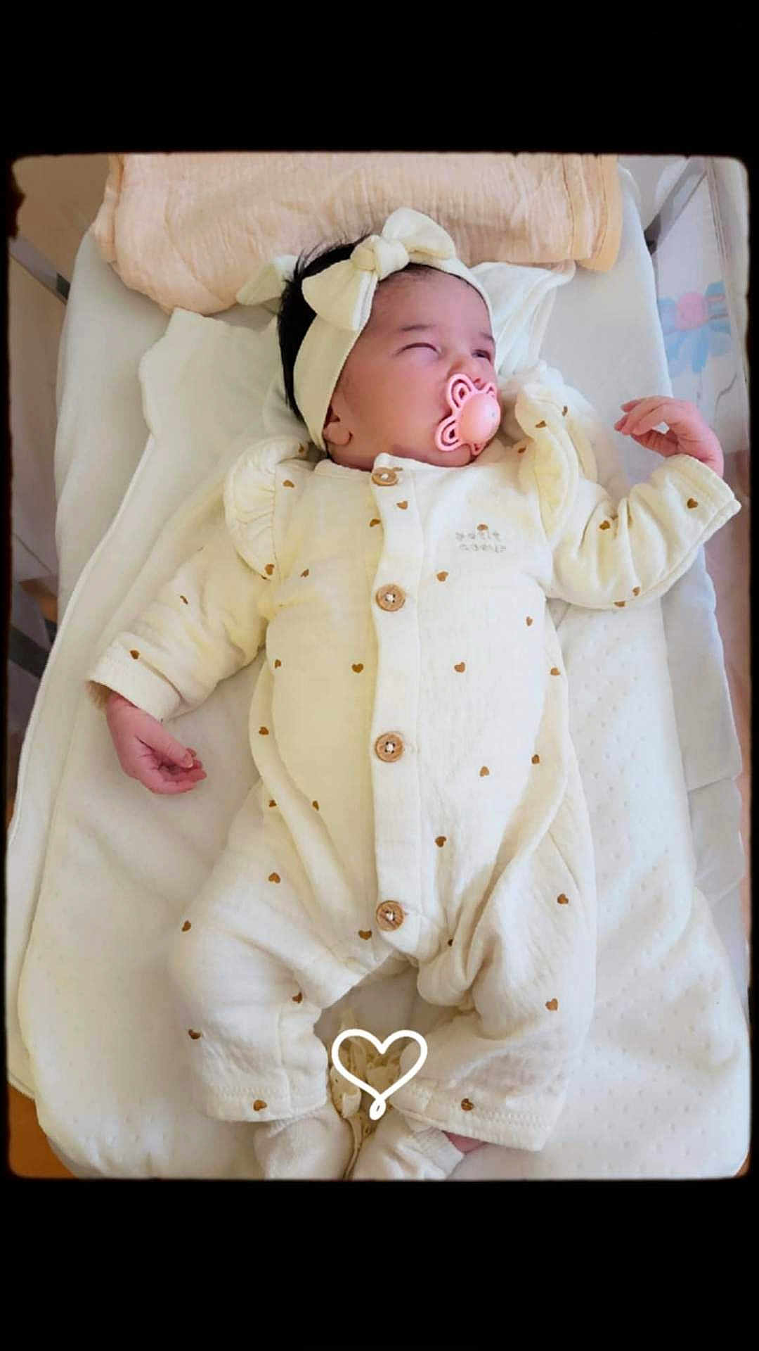 Adriana participe au concours pour gagner de l'argent avec cette photo : baby, infant, pacifier, headband, onesie, blanket, sleeping, heart_pattern, soft_toys, cozy, cute, indoor, portrait, newborn, white, pink, resting, child, clothing, peaceful