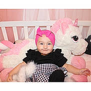 Elya participe au concours pour gagner de l'argent avec cette photo : baby, black_top, blanket, child, clothing, crib, cute, happy, headband, indoors, infant, patterned_skirt, pink, pink_bow, plush_toy, smile, soft_toy, toddler, unicorn, white