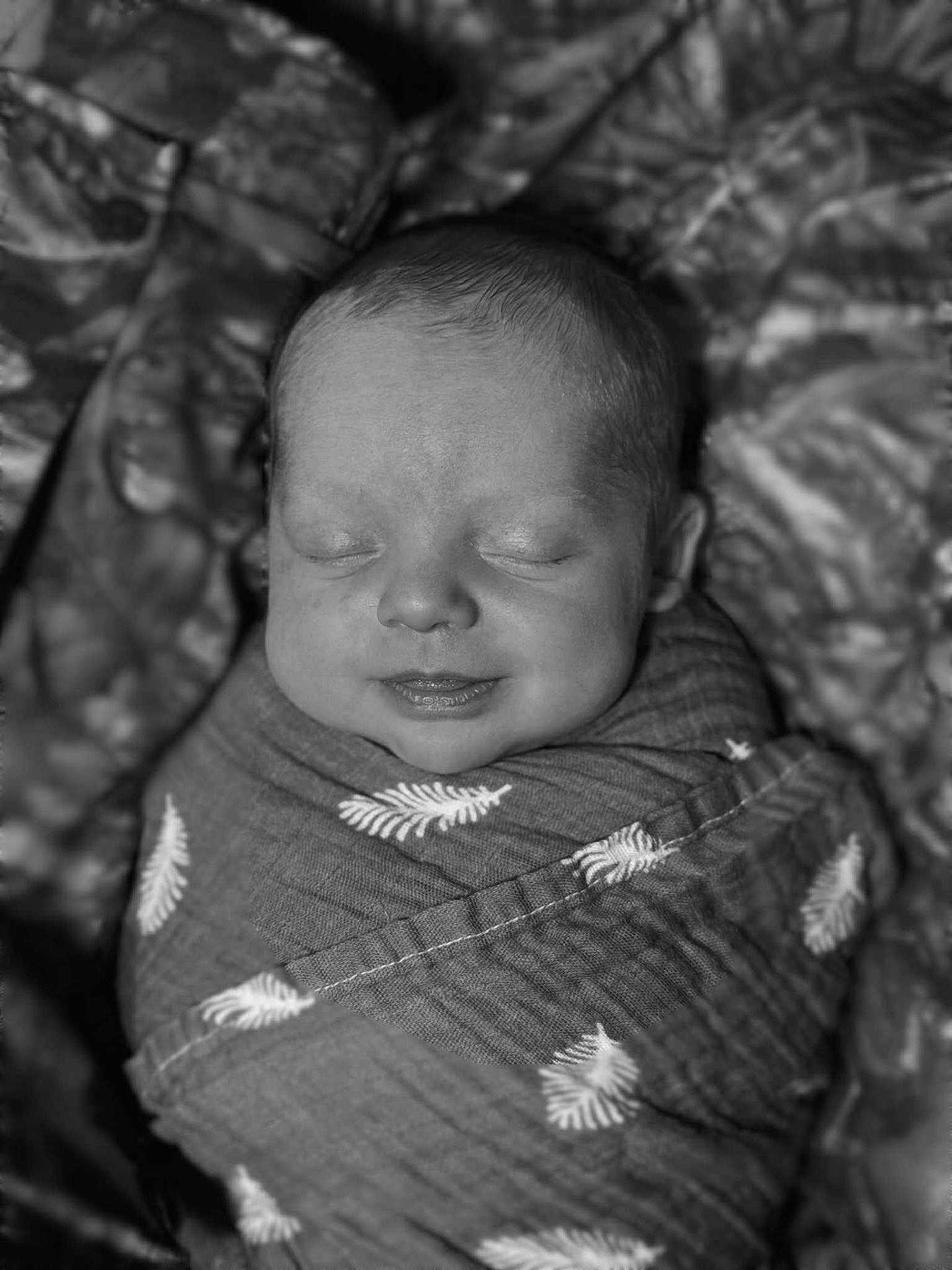 Asher is registered to the contest to win money with this photo: baby, newborn, swaddled, blanket, sleeping, smiling, face, infant, wrapped, cozy, cute, peaceful, soft, portrait, child, monochrome, black_and_white, young, resting, adorable