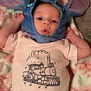 Lillianna joined the competition — help win amazing prizes! baby, infant, child, onesie, hat, costume, blue, pink, train, blanket, cute, soft, face, portrait, lying_down, indoors, expression, clothing, headwear, newborn