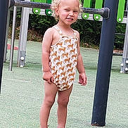 Yaël a rejoint le concours — aidez-le/la à gagner de superbes lots ! child, toddler, smiling, playground, romper, giraffe_pattern, pink_sandals, curly_hair, outdoor, green_background, metal_play_structure, happy, standing, summer_clothing, person, feet, legs, nature, daylight, recreation