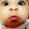 baby, close_up, face, wide_eyes, chubby_cheeks, curious_expression, hat, clothing, colorful, pattern, infant, child, portrait, cute, soft_texture, warm, indoor, young, headwear, person
