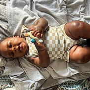 Khéphren participe au concours pour gagner de l'argent avec cette photo : baby, infant, child, toy, onesie, sock, blanket, bed, patterned_sheet, soft_texture, skin, hand, face, legs, lying_down, curious, indoor, cozy, comfort, play