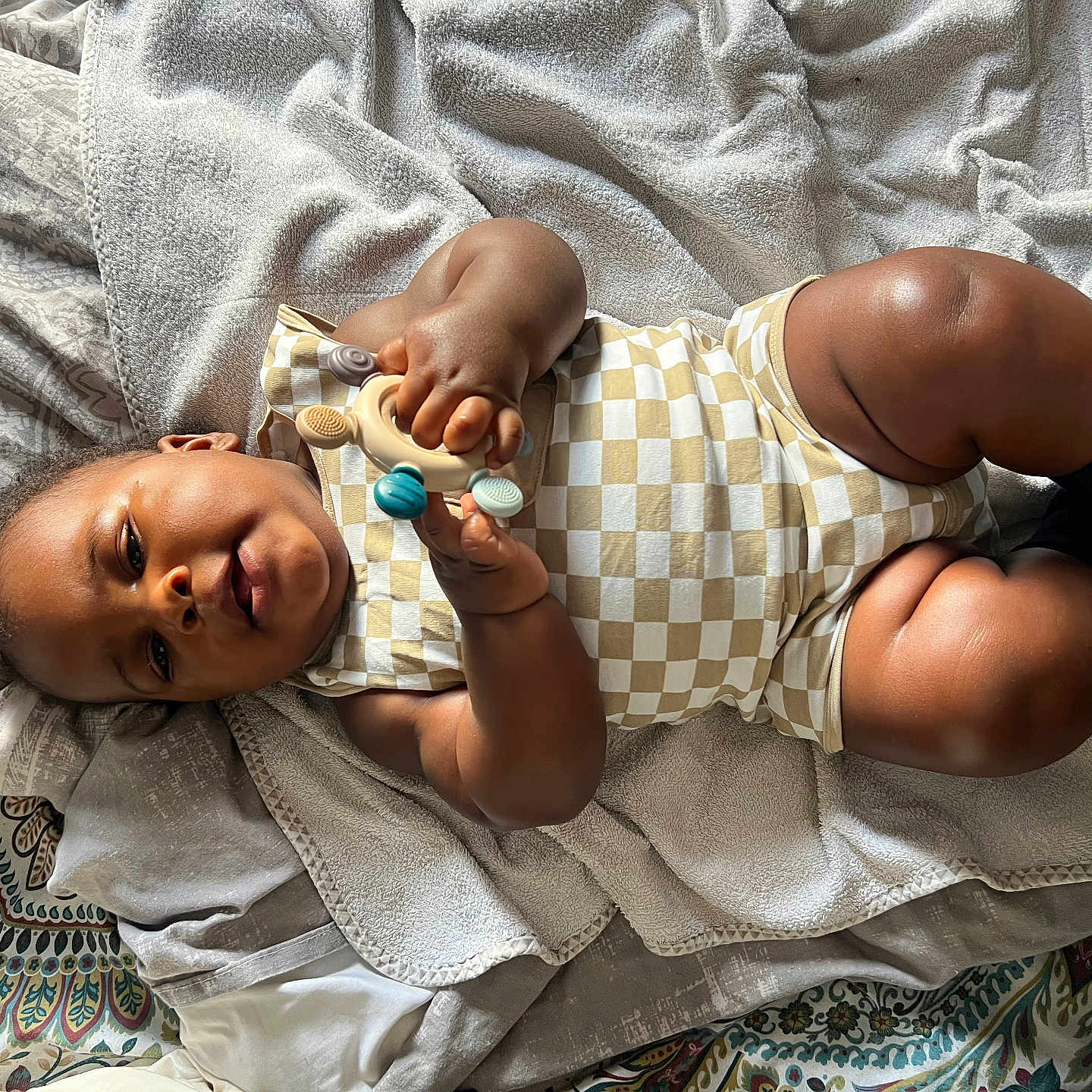 Khéphren participe au concours pour gagner de l'argent avec cette photo : baby, bed, blanket, child, comfort, cozy, curious, face, hand, indoor, infant, legs, lying_down, onesie, patterned_sheet, play, skin, sock, soft_texture, toy