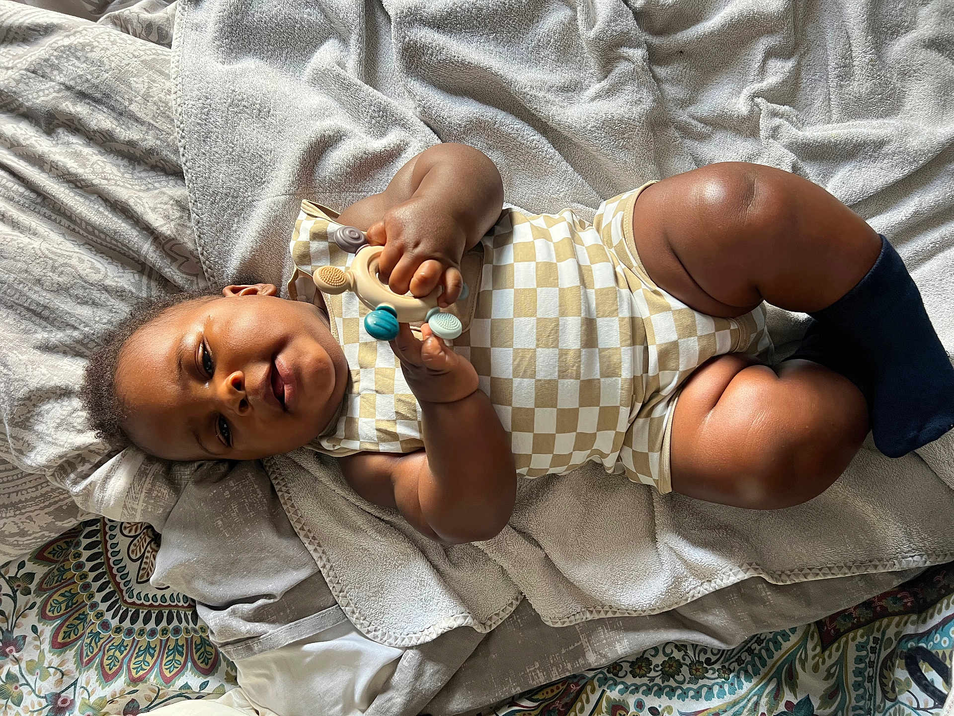 Khéphren participe au concours pour gagner de l'argent avec cette photo : baby, infant, child, toy, onesie, sock, blanket, bed, patterned_sheet, soft_texture, skin, hand, face, legs, lying_down, curious, indoor, cozy, comfort, play