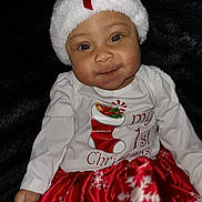 Amelia is registered to the contest to win money with this photo: baby, child, christmas, holiday, festive, hat, red_bow, white_hat, smile, red_skirt, snowflake_pattern, long_sleeve_shirt, cute, portrait, sitting, indoors, dark_background, happy, holiday_clothing, infant