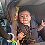 baby, car_seat, child, infant, smile, straps, seatbelt, vehicle, car_interior, clothing, button, hand, face, head, sitting, safety, cute, young_child, indoors, happy