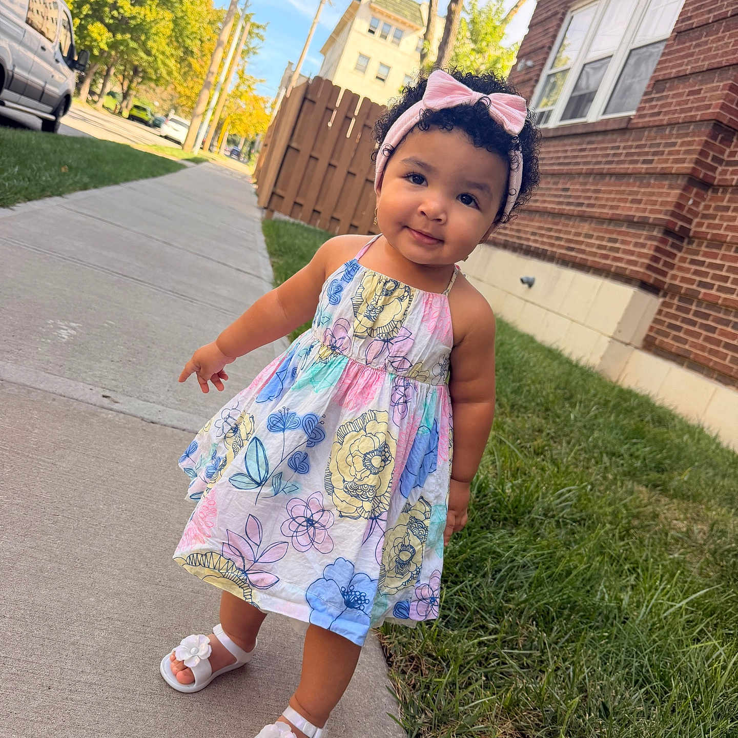 Arleth Meneses is registered to the contest to win money with this photo: toddler, child, sidewalk, dress, floral_pattern, headband, pink_bow, sandals, grass, brick_building, tree, sunlight, outdoor, curly_hair, smile, cute, urban, daytime, person, portrait