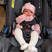 Zhamira joined the competition — help win amazing prizes! baby, child, car_seat, pink_clothing, headband, knitwear, infant, straps, seatbelt, white_socks, cute, indoors, person, portrait, sitting, small_hands, black_fabric, soft_lighting, cozy, young_child