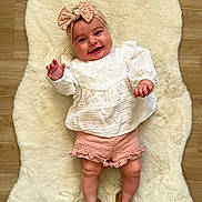 Lise participe au concours pour gagner de l'argent avec cette photo : baby, child, smiling, headband, bow, white_top, pink_shorts, ruffles, brown_shoes, fluffy_rug, wooden_floor, cute, happy, lying_down, indoors, portrait, chubby_legs, hand_raised, infant, adorable