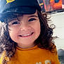 child, toddler, smiling, curly_hair, cap, hat, yellow_shirt, indoor, happy, face, cute, person, clothing, portrait, young_child, expression, joyful, childhood, casual, close_up