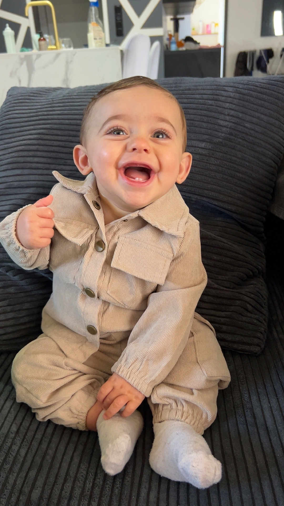 Tiago a rejoint le concours — aidez-le/la à gagner de superbes lots ! baby, child, smiling, happy, sitting, couch, clothing, beige_outfit, socks, indoor, face, portrait, young_child, joyful, cozy, hands, feet, buttoned_jacket, home_interior, fabric