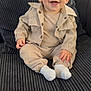 baby, child, smiling, sitting, couch, clothing, beige_outfit, white_socks, happy, indoors, face, portrait, young_child, furniture, home, cute, infant, person, joyful, cozy