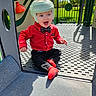 child, baby, toddler, helmet, playground, playground_equipment, red_shirt, bow_tie, black_pants, red_shoes, sitting, smiling, outdoor, sunlight, grass, park, play_structure, safety_gear, portrait, happy