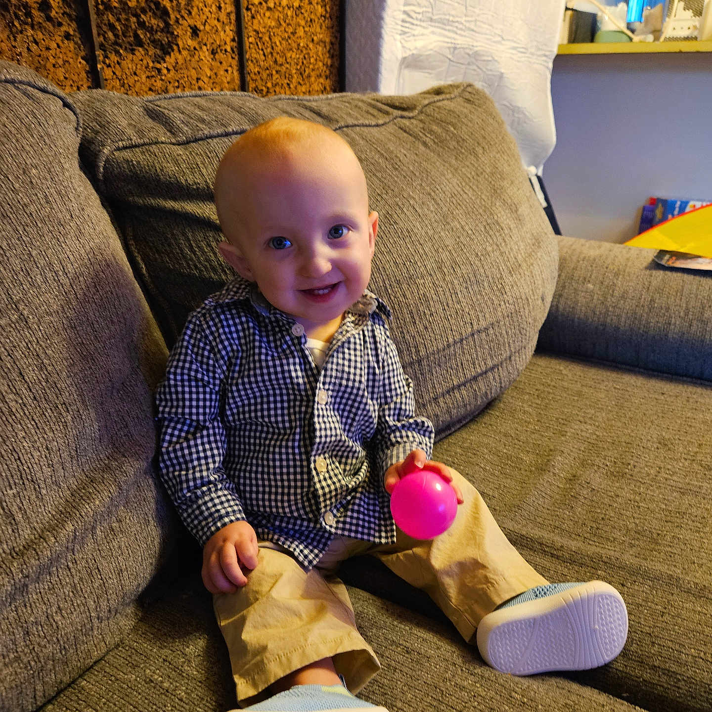 Wesley joined the competition — help win amazing prizes! baby, child, toddler, smiling, happy, portrait, sitting, couch, sofa, indoors, living_room, checkered_shirt, beige_pants, shoes, pink_ball, toy, face, blue_eyes, furniture, home