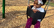 Kalaya is registered to the contest to win money with this photo: toddler, child, swing, playground, pacifier, headband, bow, outdoor, grass, trees, woodchips, shoes, pants, shirt, happy, park, person, daytime, recreation, fun