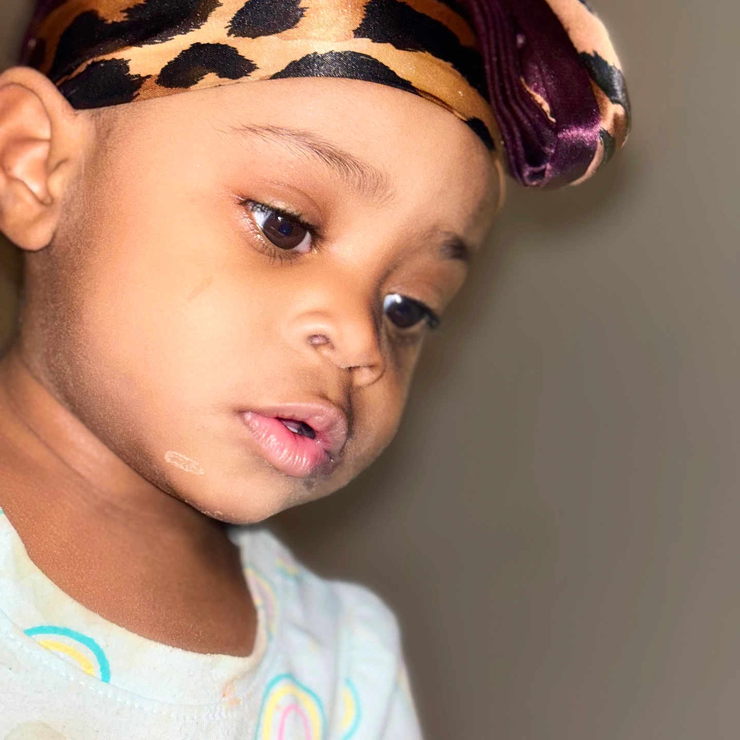 Kalaya is registered to the contest to win money with this photo: toddler, child, portrait, headscarf, leopard_print, bow, close_up, face, skin, expression, looking_down, clothing, rainbow_pattern, soft_lighting, indoor, young_child, person, cute, baby, headwear
