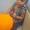 toddler, child, baby, blue_headband, orange_ball, sitting, couch, curious, happy, indoor, clothing, patterned_dress, legs, hand, face, smile, person, young_child, cute, portrait