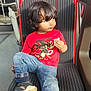 bus, casual, child, curly_hair, daylight, indoors, jeans, people, portrait, public_transport, red_shirt, relaxed, sandals, seat, side_glance, snack, striped_seat, toddler, window, young_child
