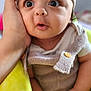 baby, button, child, clothing, cute, expression, eyes, face, hand, indoors, infant, knit_hat, mouth, person, portrait, sitting, skin, soft_texture, surprised, yellow_blanket