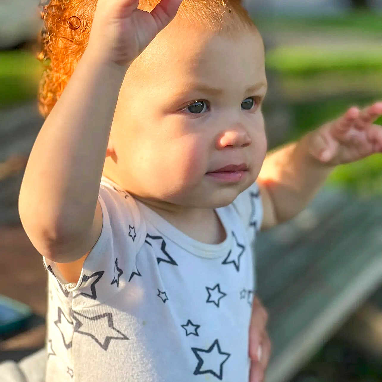 Shaya joined the competition — help win amazing prizes! bench, blurred_background, child, curly_hair, cute, daylight, expression, face, hands, innocent, nature, outdoor, person, portrait, red_hair, shirt, star_pattern, sunlight, toddler, young_child