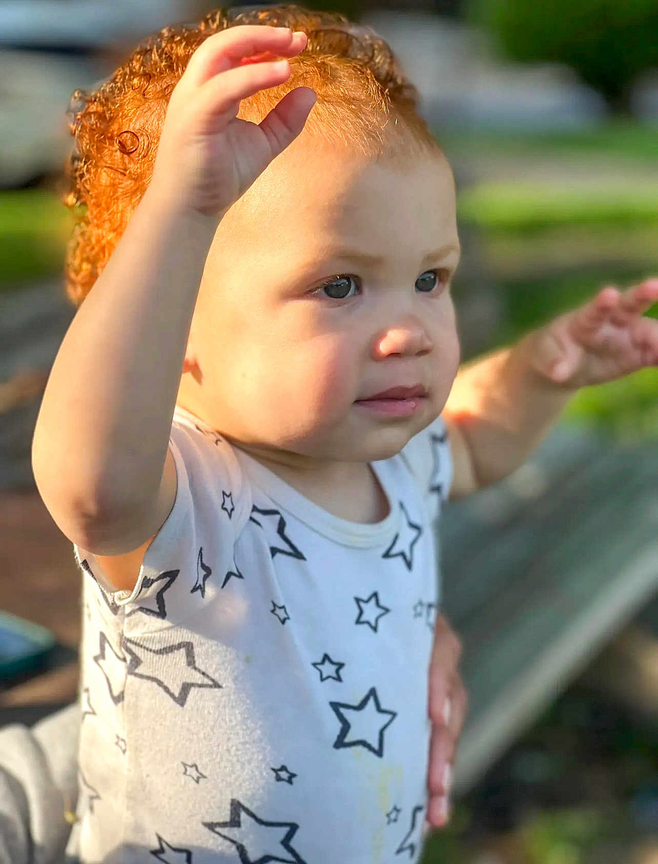 Shaya joined the competition — help win amazing prizes! toddler, child, curly_hair, red_hair, star_pattern, shirt, outdoor, sunlight, portrait, face, hands, expression, young_child, person, nature, bench, blurred_background, cute, innocent, daylight