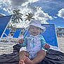 baby, child, beach, sun_hat, swimsuit, towel, beach_chair, sand, palm_trees, sky, clouds, smiling, happy, outdoor, vacation, summer, sunny, person, foot, hand