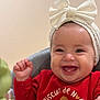 Liva a rejoint le concours — aidez-le/la à gagner de superbes lots ! baby, child, infant, smiling, headband, bow, red_sweater, gingerbread_print, teeth, cheeks, hand, toy, highchair, portrait, close_up, happy, indoor, soft_background, eyes, skin