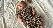 Magnolia is registered to the contest to win money with this photo: baby, bed, blanket, child, comfort, curious, cute, floral_pattern, headband, indoor, infant, lying_down, newborn, person, portrait, romper, soft_texture, three_months, white, wooden_sign