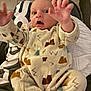 baby, infant, onesie, mountain_pattern, clothing, person, hand, face, expression, indoor, floor, tile, lap, sitting, young_child, cute, wide_eyes, open_mouth, reaching, cozy