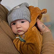 Malone participe au concours pour gagner de l'argent avec cette photo : baby, child, knitted_hat, bear_costume, pacifier, adult_hand, warm_clothing, indoor, portrait, cute, soft_texture, close_up, cozy, toddler, face, expression, holding, person, infant, winter