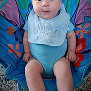 Elijah is registered to the contest to win money with this photo: baby, infant, child, blue_onesie, bib, baby_chair, colorful, indoor, carpet, curious, face, legs, feet, hands, person, cute, portrait, sitting, young, expression