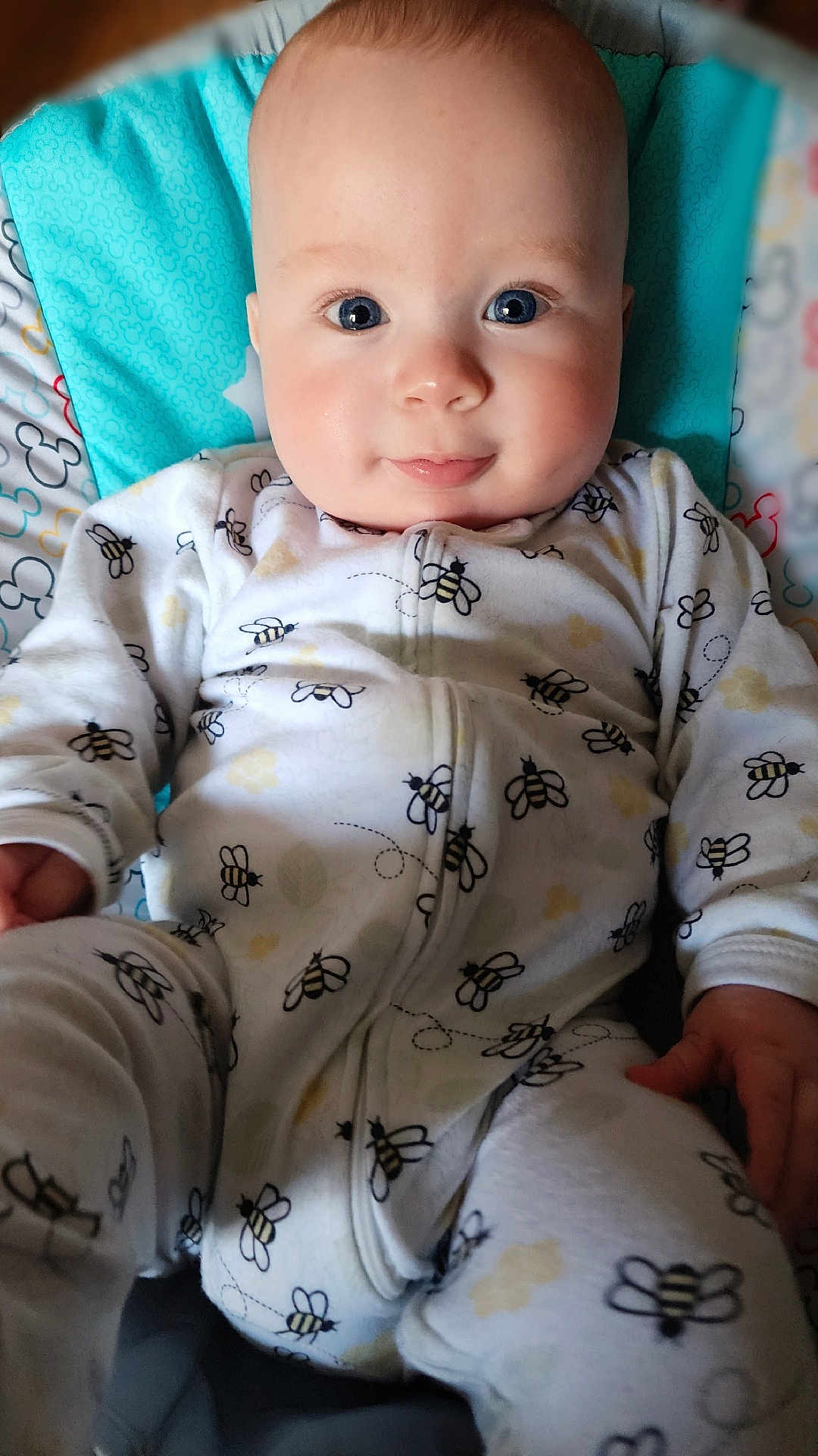 Elijah is registered to the contest to win money with this photo: baby, infant, onesie, bee_pattern, blue_cushion, smiling, face, eyes, hand, sitting, child, cute, comfort, clothing, indoors, portrait, skin, head, person, background_blur