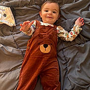 Colton joined the competition — help win amazing prizes! baby, child, overalls, brown_clothing, bear_design, blanket, gray_blanket, bed, smiling, reaching_hand, cute, indoor, infant, person, happy, cozy, clothing, long_sleeve_shirt, patterned_shirt, lying_down