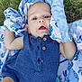 baby, blanket, blue_outfit, child, close_up, curious_expression, daylight, face, grass, head, infant, lying_down, nature, outdoor, person, plush_blanket, skin, soft_texture, summer, wooden_buttons