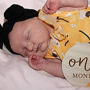 Justina joined the competition — help win amazing prizes! baby, infant, sleeping, headband, bow, yellow_dress, floral_pattern, milestone_sign, one_month, soft_blanket, newborn, peaceful, close_up, portrait, cute, hands, skin, face, resting, photography