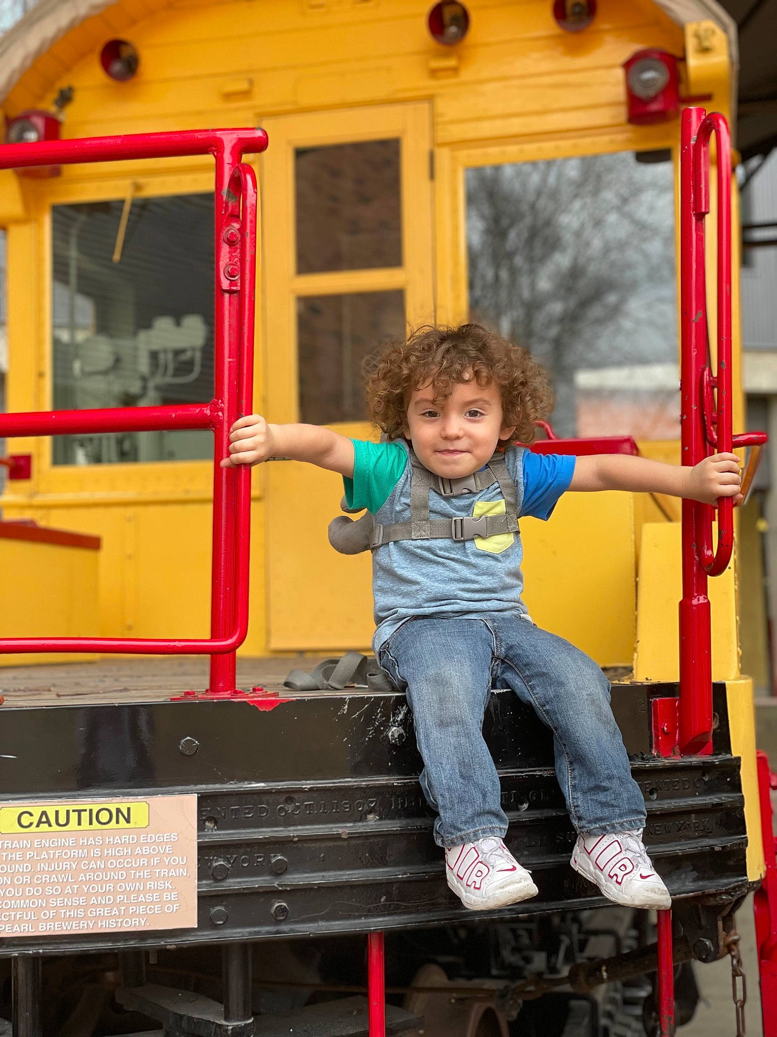 Graysen is registered to the contest to win money with this photo: child, city, fun, joy, leisure, mode_of_transport, motor_vehicle, outdoor_play_equipment, person, playground, public_space, recreation, red, rolling, shorts, smile, standing, t_shirt, toddler, vehicle
