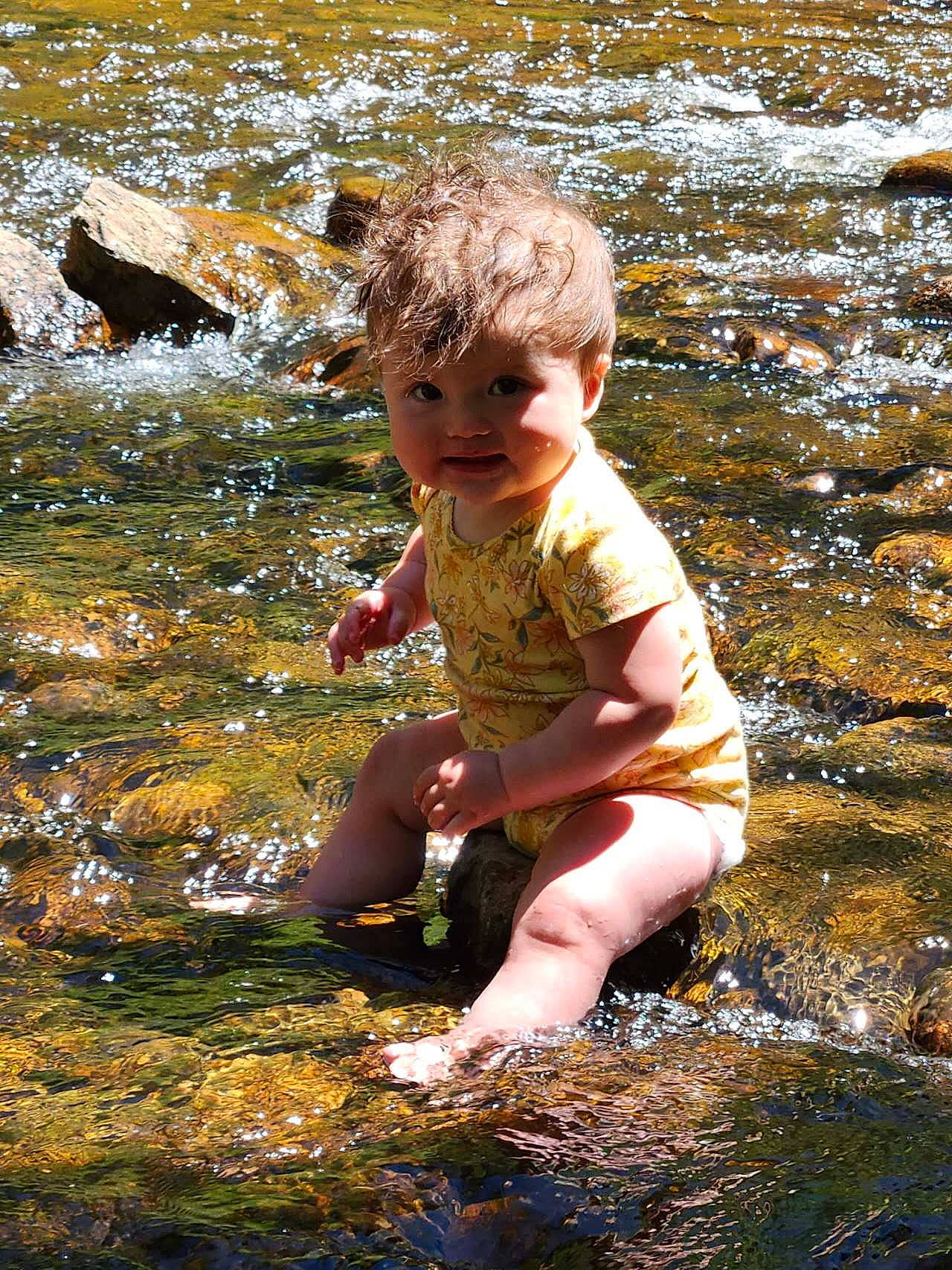 Arianna joined the competition — help win amazing prizes! bank, barefoot, body_of_water, child, fun, grass, happy, leaf, leisure, people_in_nature, person, reflection, rock, sitting, stream, sunlight, toddler, vacation, water, watercourse