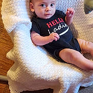 Logan Forrest is registered to the contest to win money with this photo: baby, infant, blanket, onesie, text, floor, wooden_floor, indoor, person, face, skin, hand, foot, clothing, cute, young_child, laying_down, texture, comfortable, expression