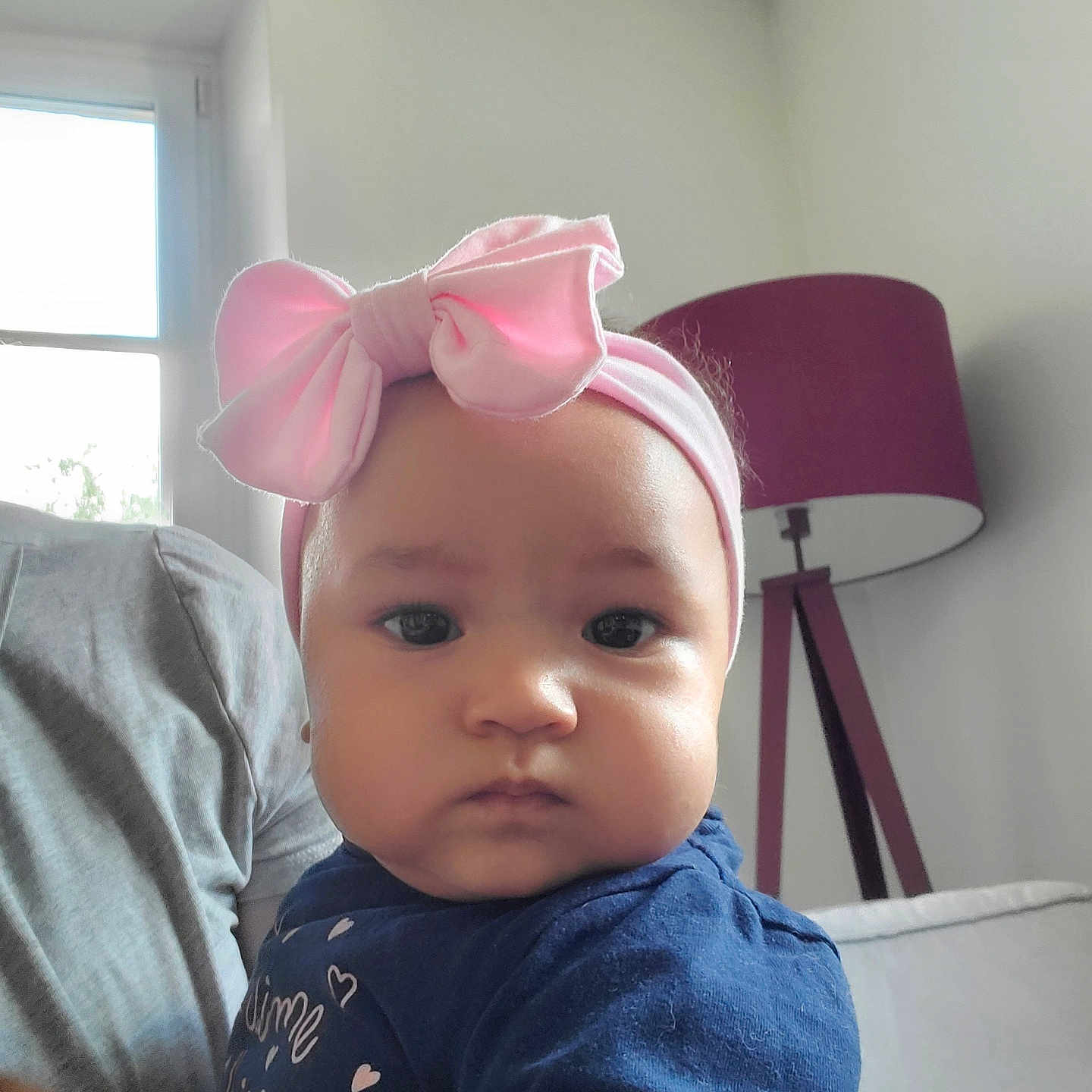 Nanisca participe au concours pour gagner de l'argent avec cette photo : adult_hand, baby, blue_clothing, child, closeup, couch, expressionless, face, headband, home, human, indoor, infant, lamp, light, person, pink_bow, portrait, sitting, window